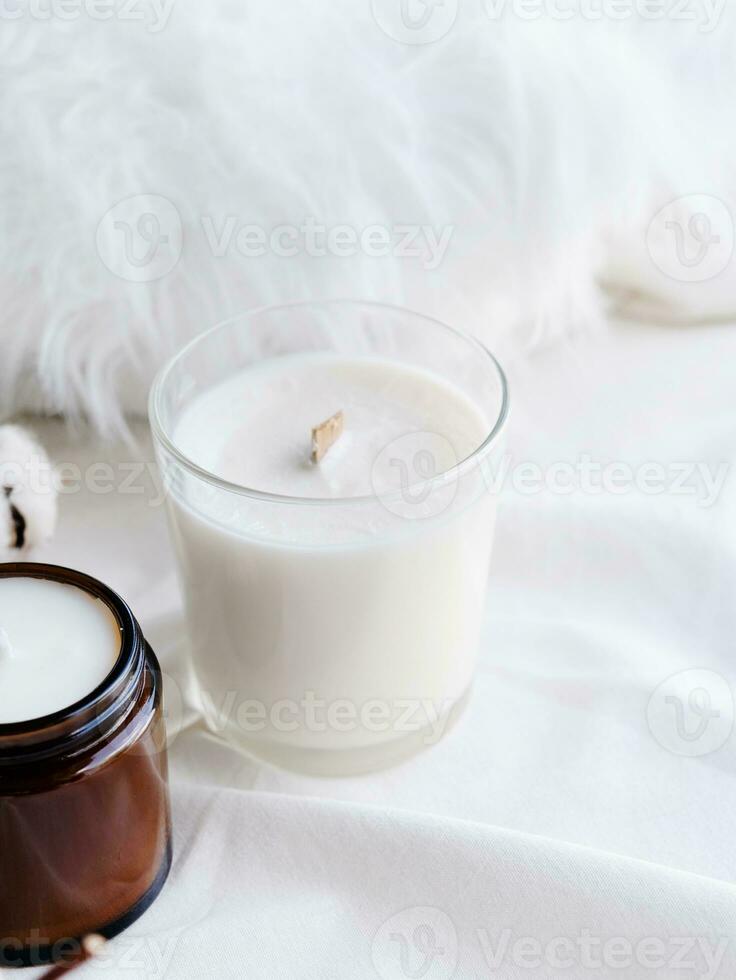 Soy wax aroma candle in white jar on bed with cotton branch. Candle mockup design photo