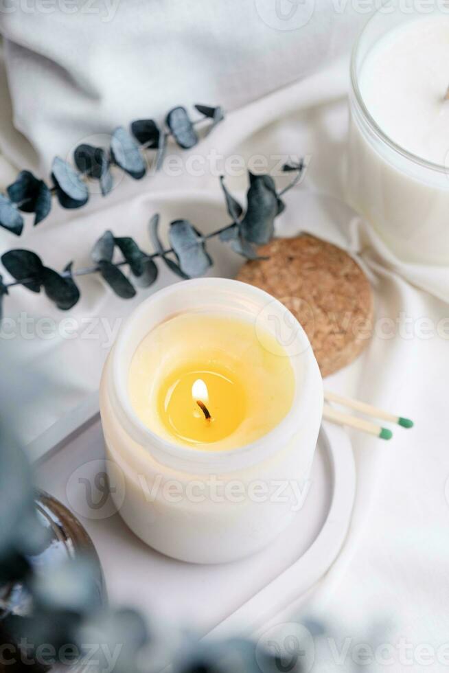 Soy wax aroma candle in white jar on bed with eucalyptus leaves. Candle mockup design photo