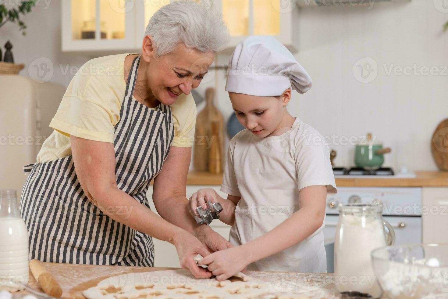 Happy family in kitchen. Grandmother granddaughter child cutting cookies of dough on kitchen table together. Grandma teaching kid girl cook bake cookies. Household teamwork helping family generations. photo
