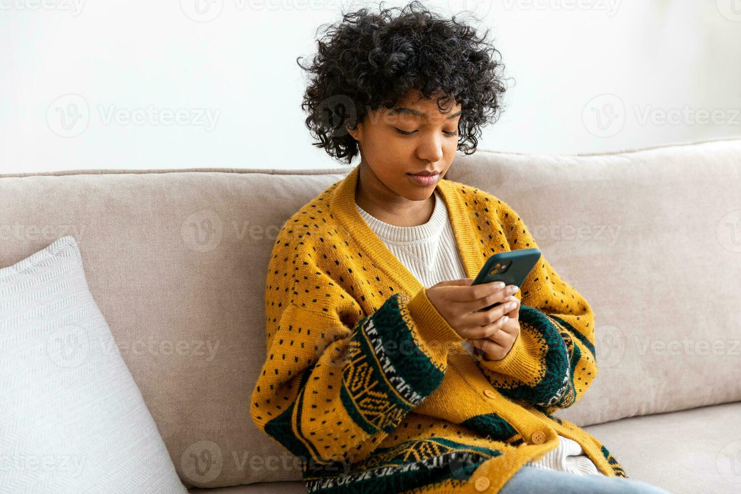 African girl holding smartphone touch screen typing scroll page at home. Woman with cell phone surfing internet using social media apps playing game. Shopping online Internet news cellphone addiction. photo