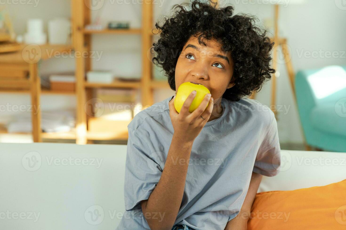 Happy pretty girl biting green apple at home. Beautiful african american young woman eating fresh fruit and smiling. Healthy food vegan vegetarian dieting concept. Healthy snack clean food. photo