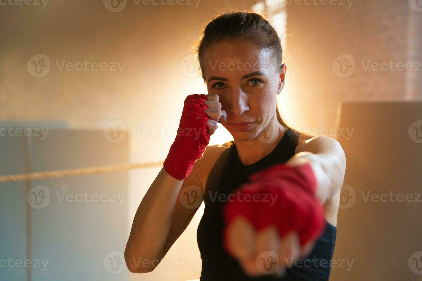 Women self defense girl power. Strong woman fighter punching with red boxing wraps sports protective bandages. Girl punching training punches looking concentrated straight. Fit body workout. photo