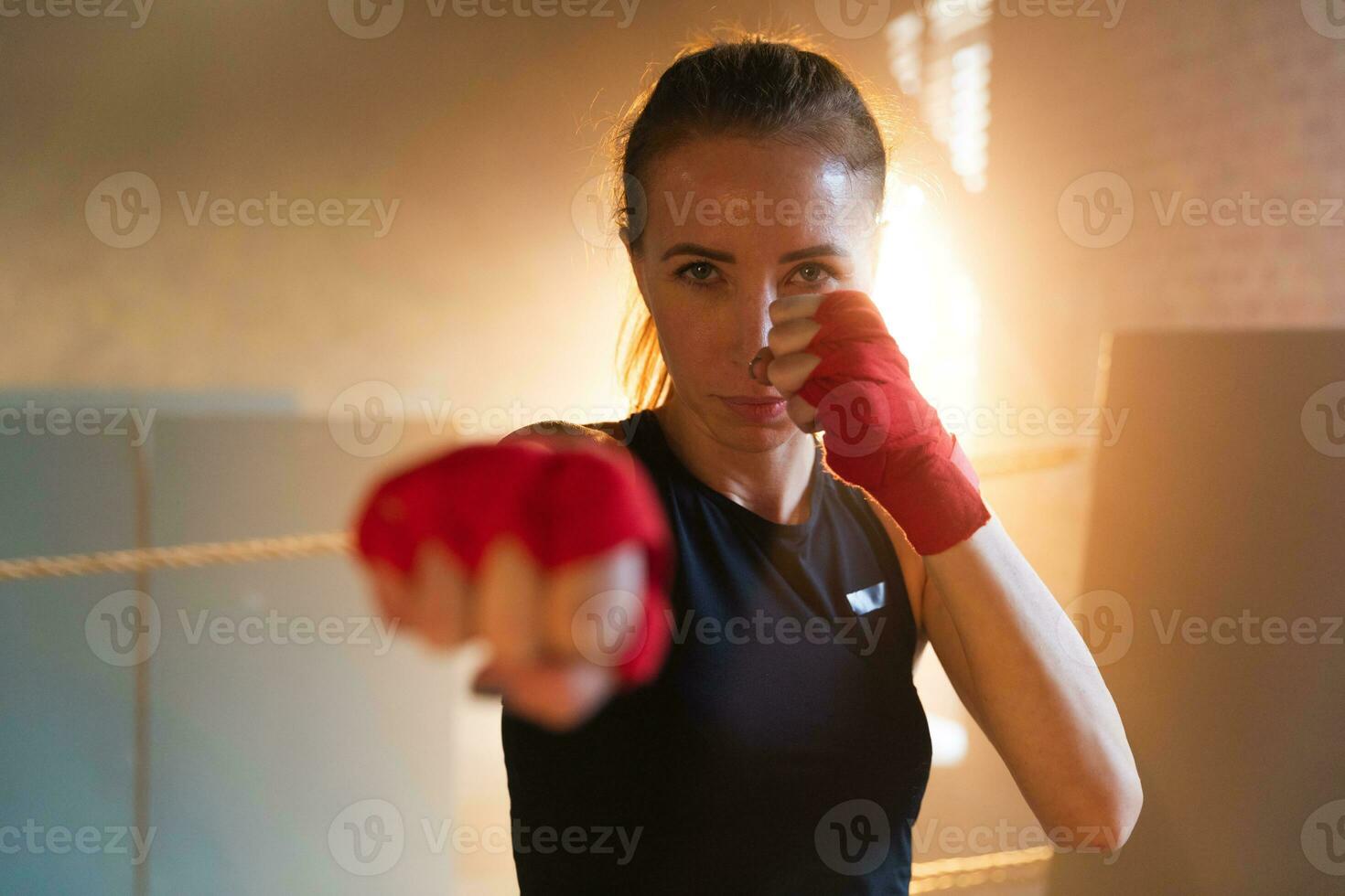 Women self defense girl power. Strong woman fighter punching with red boxing wraps sports protective bandages. Girl punching training punches looking concentrated straight. Fit body workout. photo