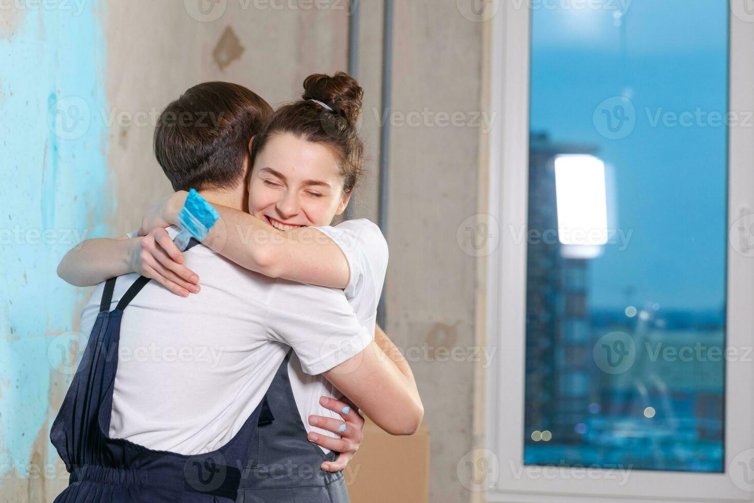 House decoration DIY renovation concept. Happy couple during repair in empty room of new home painting wall together. Husband and wife hugging in new house. Happy family doing home renovation. photo