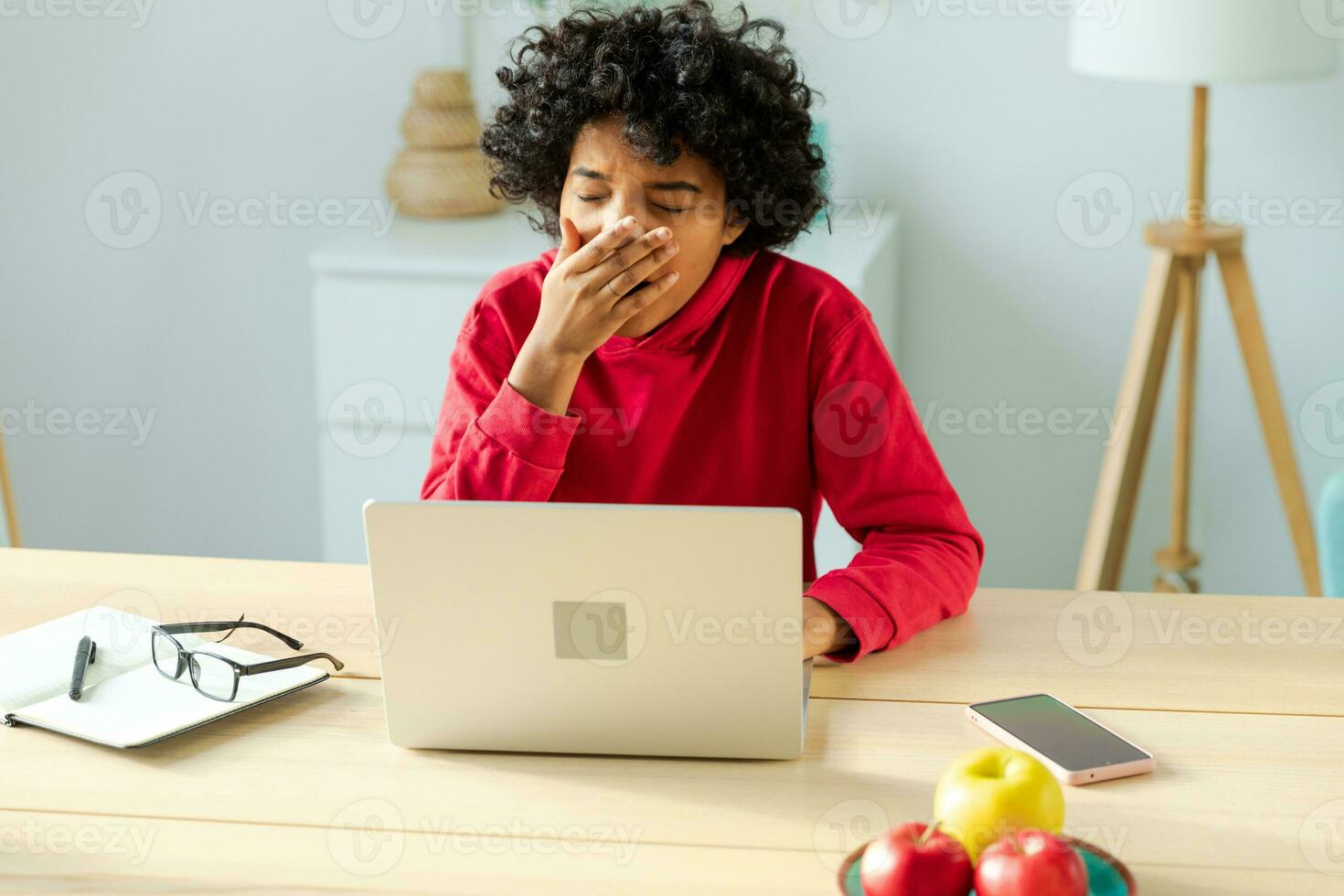 Sleepy african american woman sitting at table with laptop and yawning. Tired overworked girl lazy to work. Student businesswoman relaxing bored in home office after work on laptop computer. photo