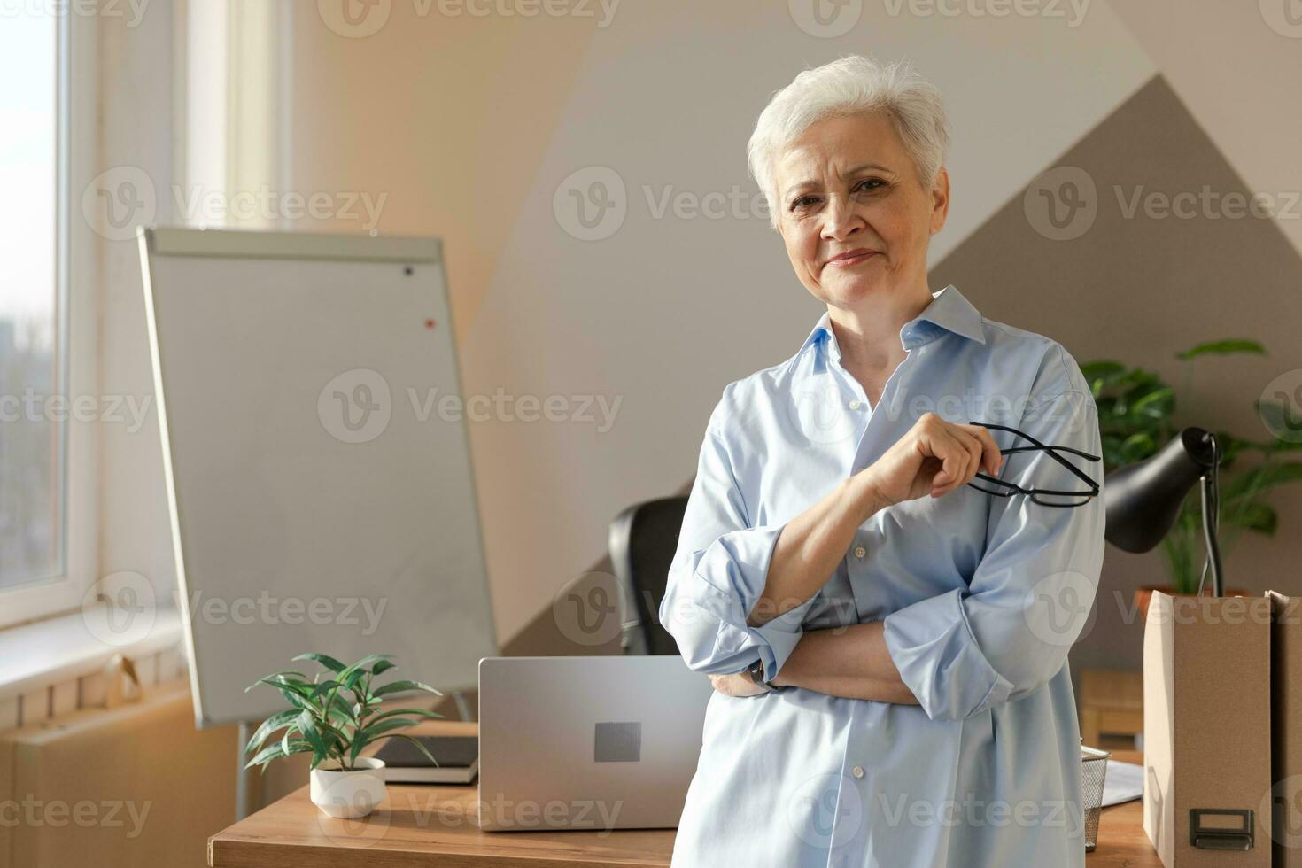 Portrait of confident stylish european middle aged senior woman at workplace. Stylish older mature 60s gray haired lady businesswoman in modern office. Boss leader teacher professional worker. photo