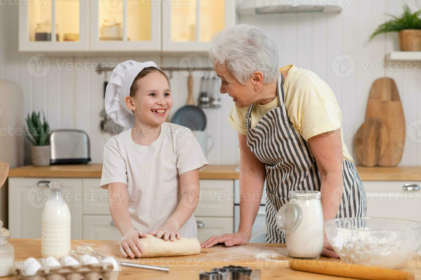 Happy family in kitchen. Grandmother and granddaughter child cook in kitchen together. Grandma teaching kid girl knead dough bake cookies. Household teamwork helping family generations concept. photo