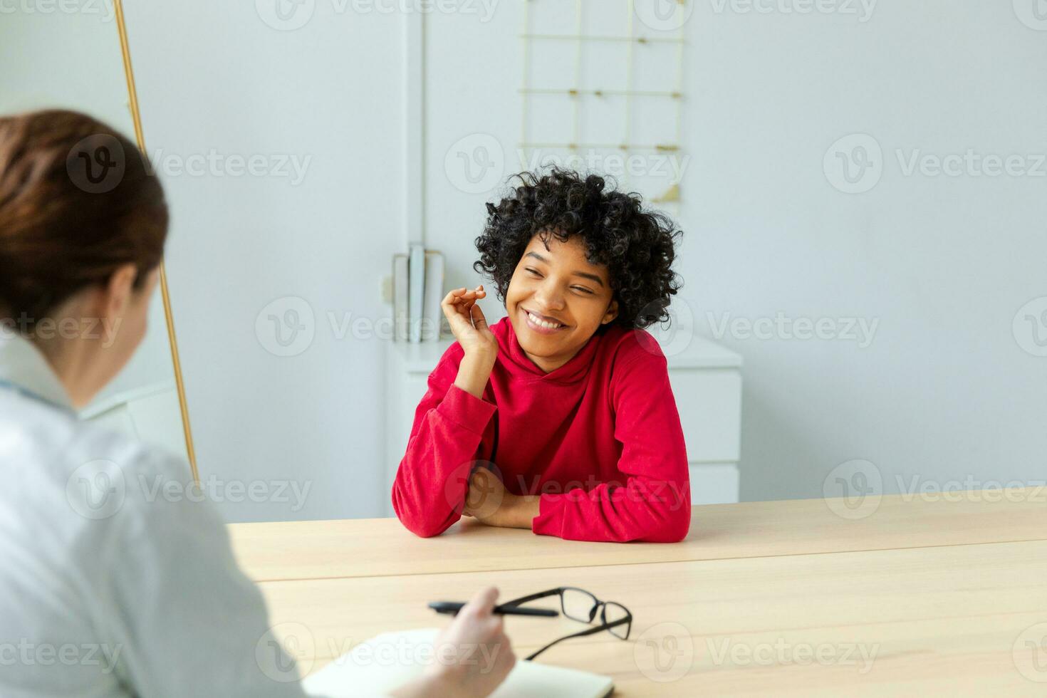 Young african american woman patient and female doctor in doctor office. Girl patient and doctor have consultation in hospital room. Medicine healthcare medical checkup concept. Visit to doctor. photo