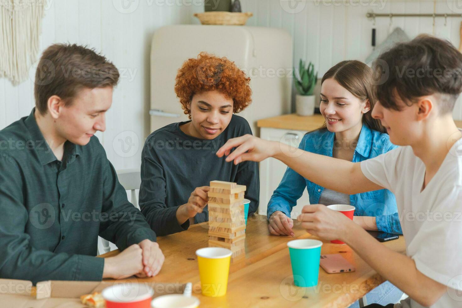 Home party. Friends spending time together playing in board game crash wooden tower at home. Happy diverse group having fun together indoor. Mixed race young buddies best friends enjoying weekend. photo