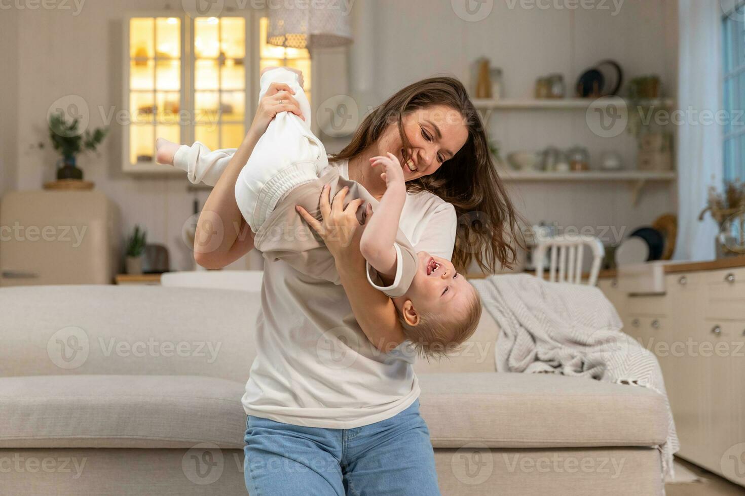 Happy family at home. Mother lifting in air little toddler child son. Mom and baby boy playing having fun together at home. Mother hugs baby with love care. Young mother kid son rest in living room. photo