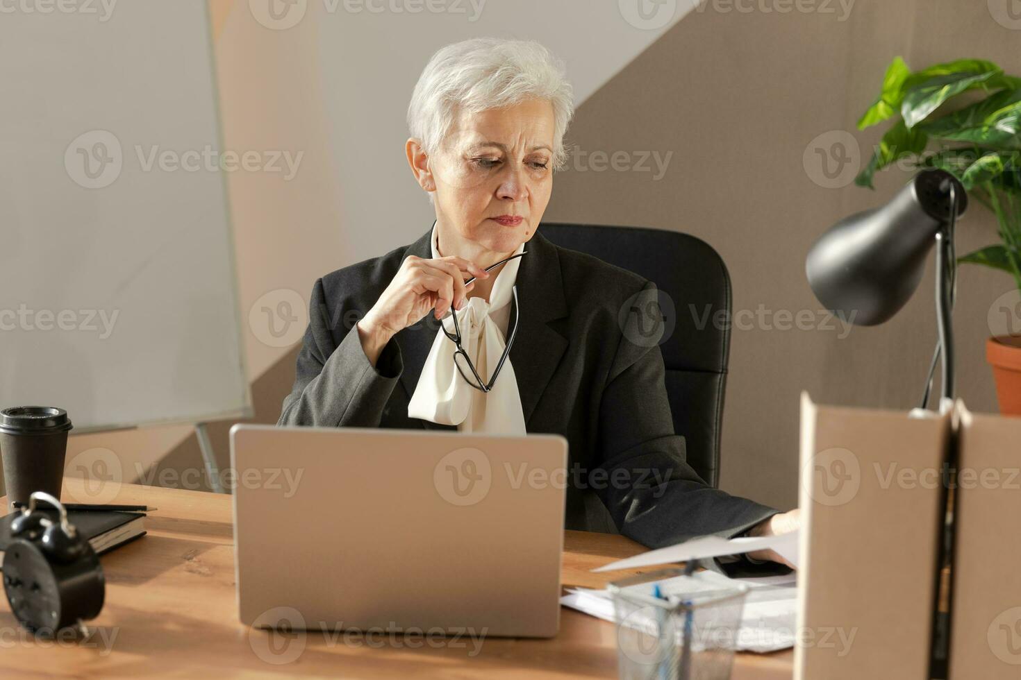 Confident stylish european middle aged senior woman reading financial report documentation statistics. Stylish older mature 60s gray haired lady businesswoman in office. Boss leader teacher. photo