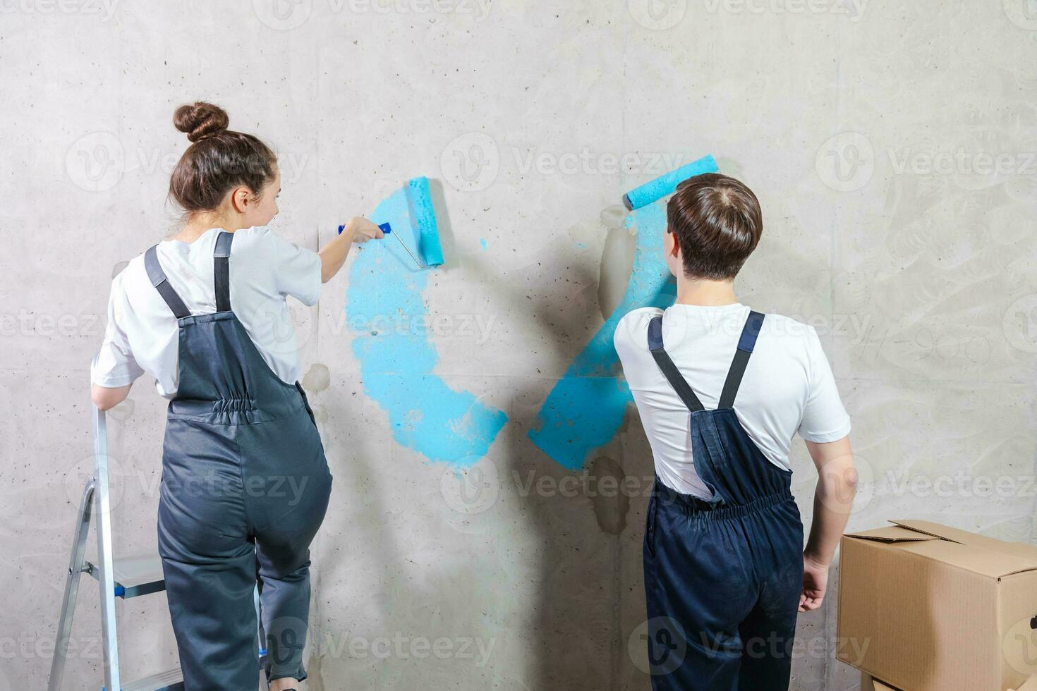 Couple in new home during repair works painting wall together. Happy family holding paint roller painting wall with blue color paint in new house. Home renovation DIY renew home concept. photo