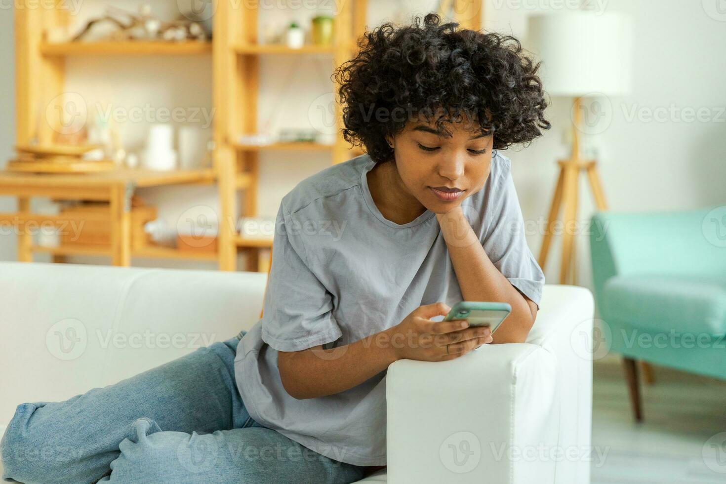 African girl holding smartphone touch screen typing scroll page at home. Woman with cell phone surfing internet using social media apps playing game. Shopping online Internet news cellphone addiction. photo