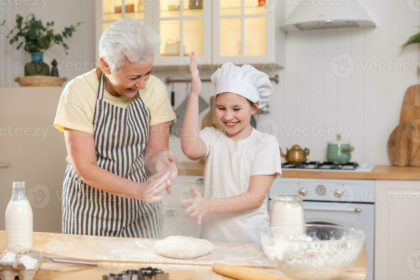 contento familia en cocina. abuela y nieta niño cocinar en cocina juntos. abuela enseñando niño niña amasar masa hornear galletas. casa trabajo en equipo Ayudar familia generaciones concepto. foto