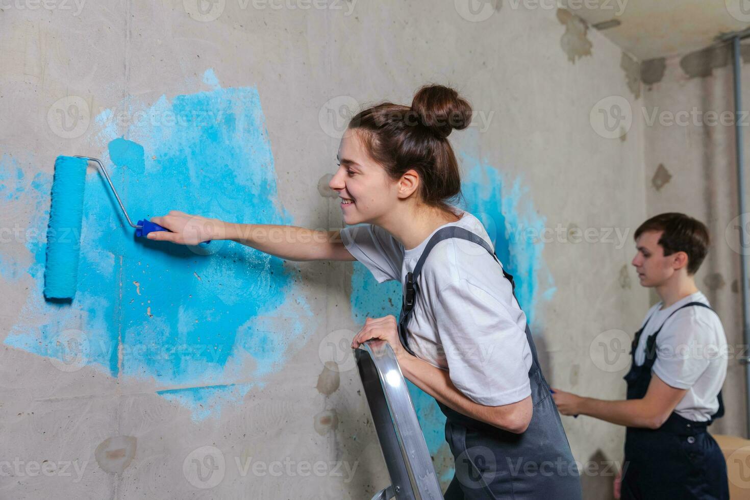 Couple in new home during repair works painting wall together. Happy family holding paint roller painting wall with blue color paint in new house. Home renovation DIY renew home concept. photo