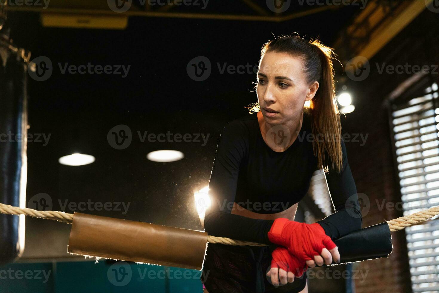 Woman fighter girl power. Woman fighter with red boxing wraps protective bandages standing on boxing ring leaning on ropes waiting resting. Strong powerful girl. Strength fit body workout training. photo