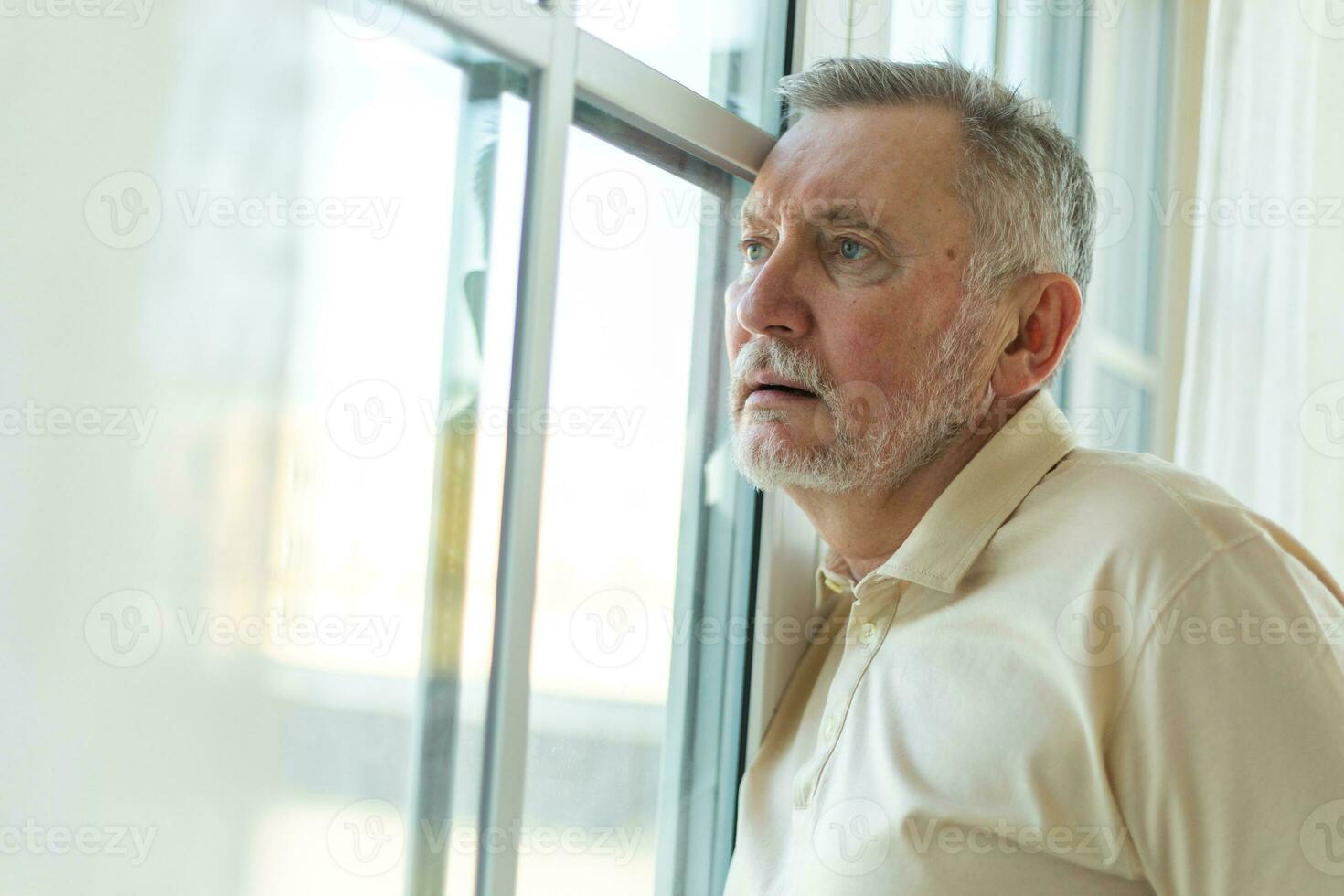 Sad tired lonely disappointed older senior man at home alone. Unhappy grandfather looking sadly outside window experiencing grief relative death bad news. Stressed elder man suffering from loneliness. photo