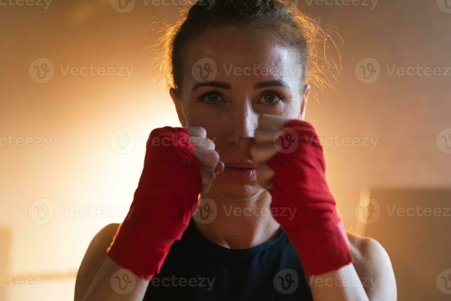 Women self defense girl power. Strong woman fighter punching with red boxing wraps sports protective bandages. Girl punching training punches looking concentrated straight. Fit body workout. photo