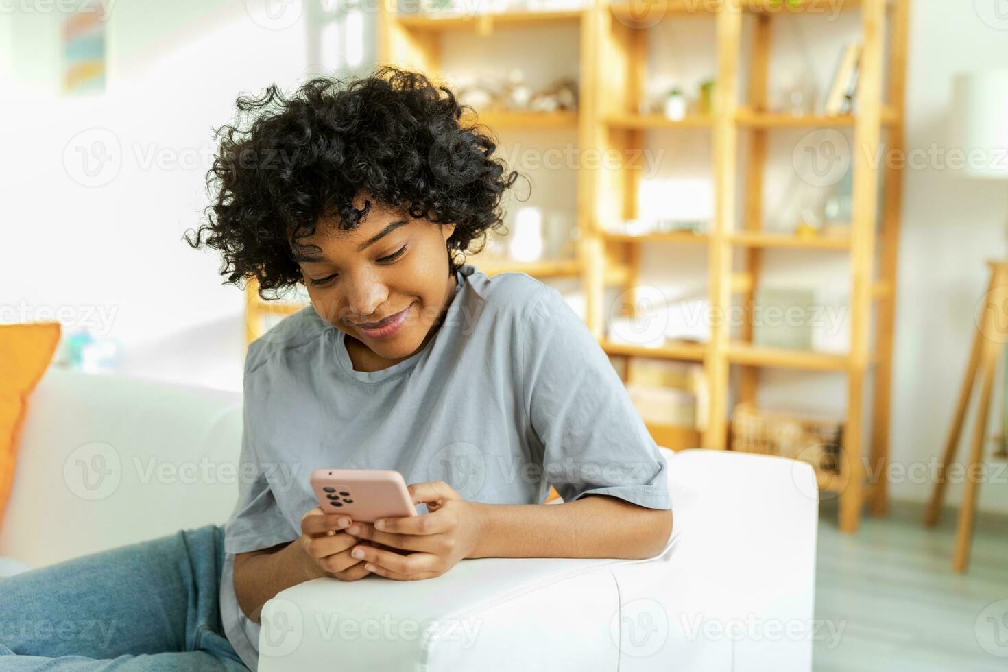African girl holding smartphone touch screen typing scroll page at home. Woman with cell phone surfing internet using social media apps playing game. Shopping online Internet news cellphone addiction. photo