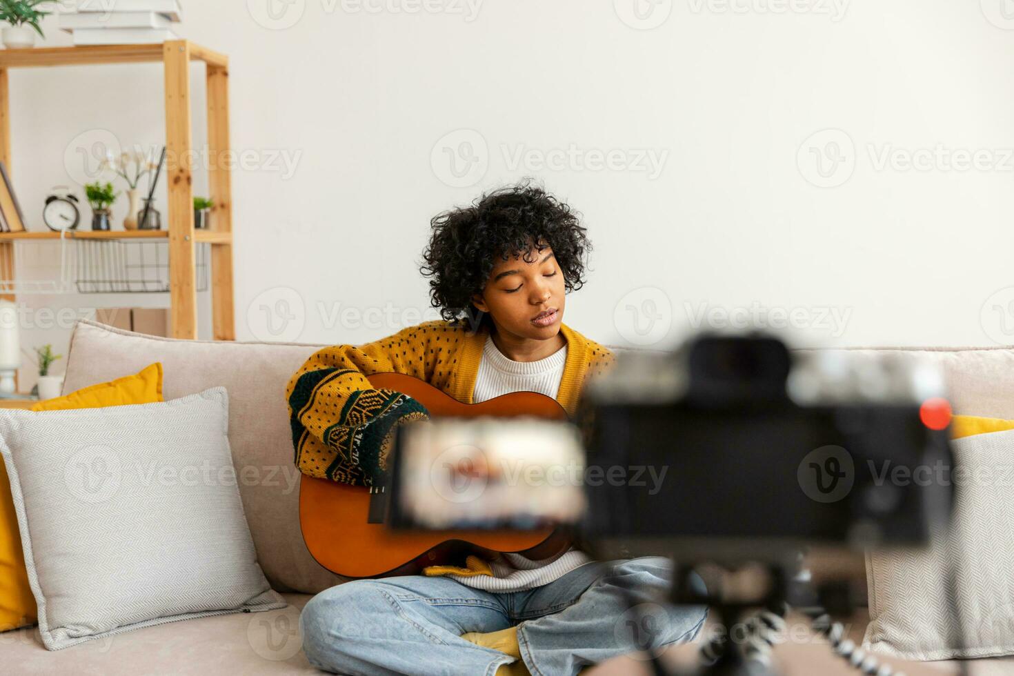 Blogger guitarist. African american girl blogger playing guitar talking to webcam recording vlog. Social media influencer woman streaming at home indoors. Music content creator broadcast tutorial. photo