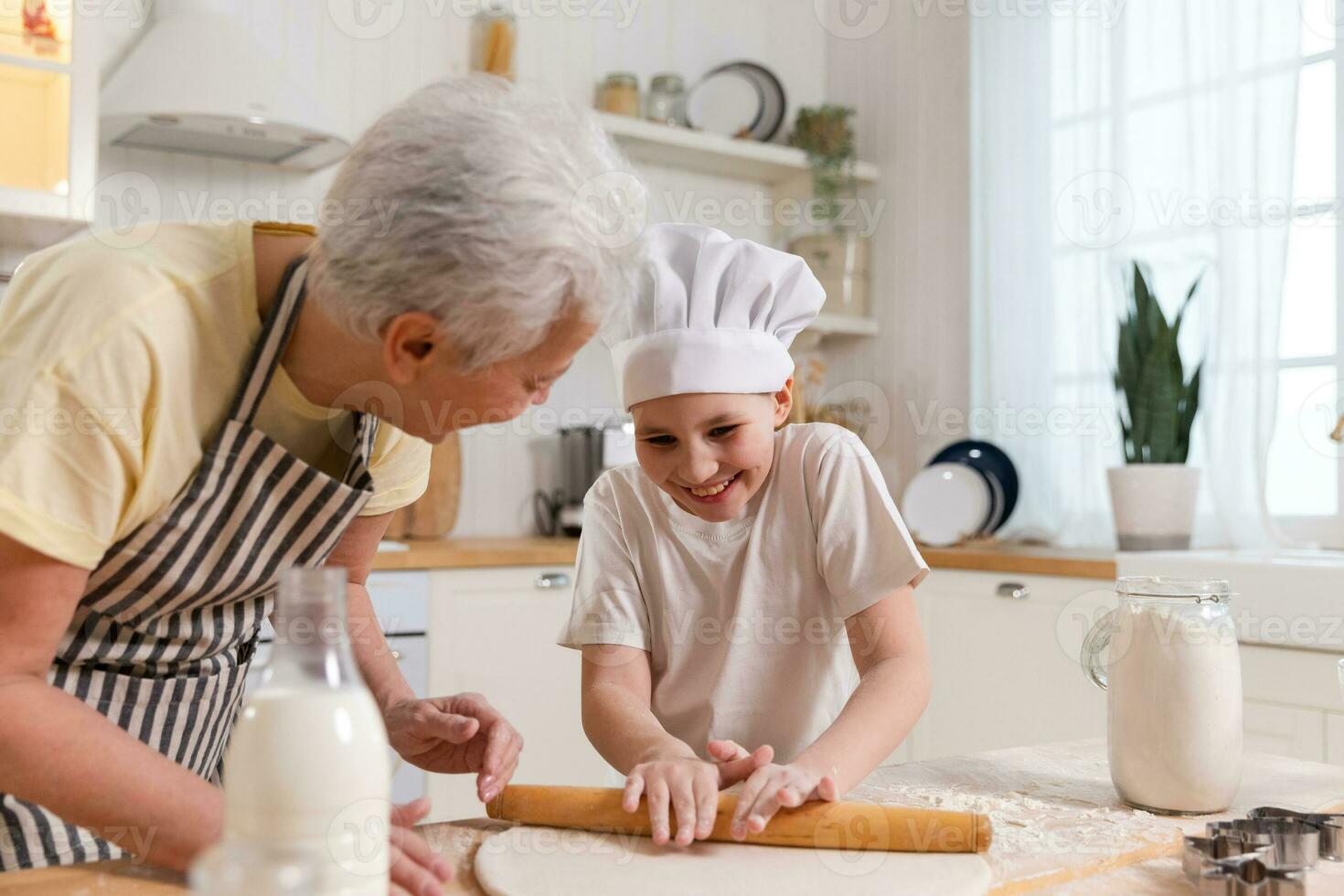 Happy family in kitchen. Grandmother and granddaughter child cook in kitchen together. Grandma teaching kid girl roll out dough bake cookies. Household teamwork helping family generations concept. photo