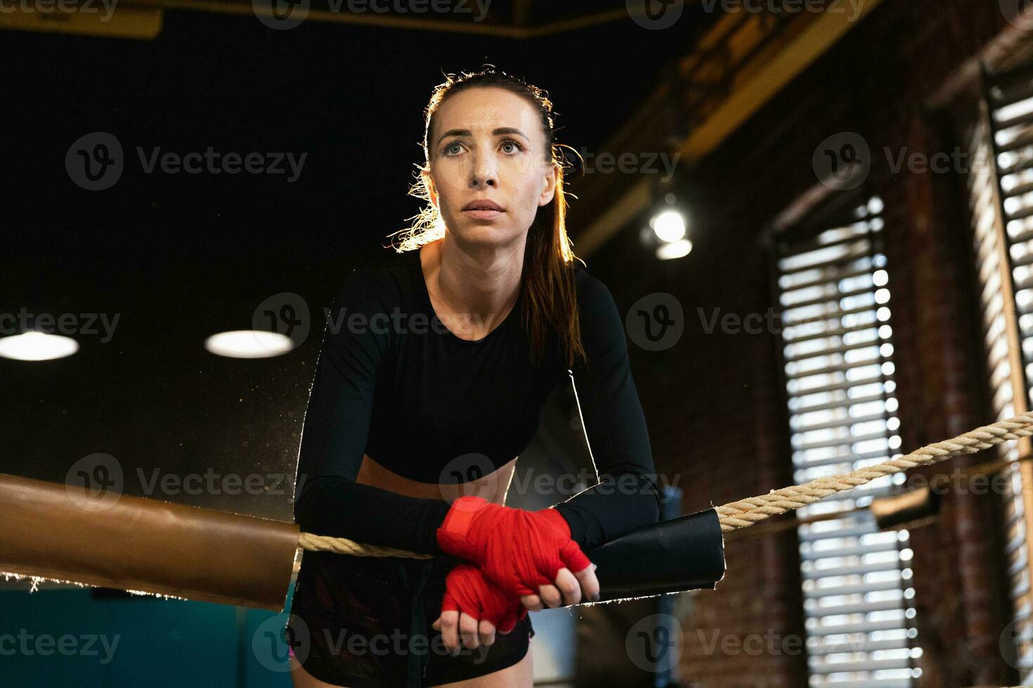 Woman fighter girl power. Woman fighter with red boxing wraps protective bandages standing on boxing ring leaning on ropes waiting resting. Strong powerful girl. Strength fit body workout training. photo