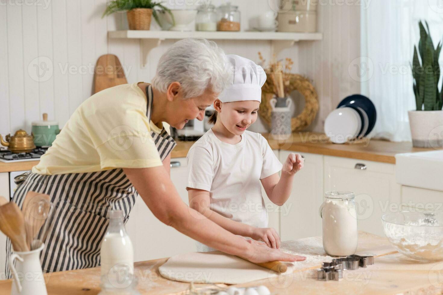 Happy family in kitchen. Grandmother and granddaughter child cook in kitchen together. Grandma teaching kid girl roll out dough bake cookies. Household teamwork helping family generations concept. photo