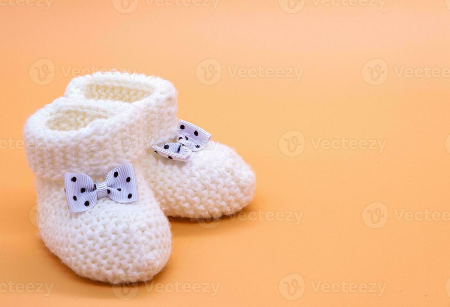 Knitted white baby booties with bows in black polka dots on a delicate orange isolated background. Background. For text. Photo in high quality