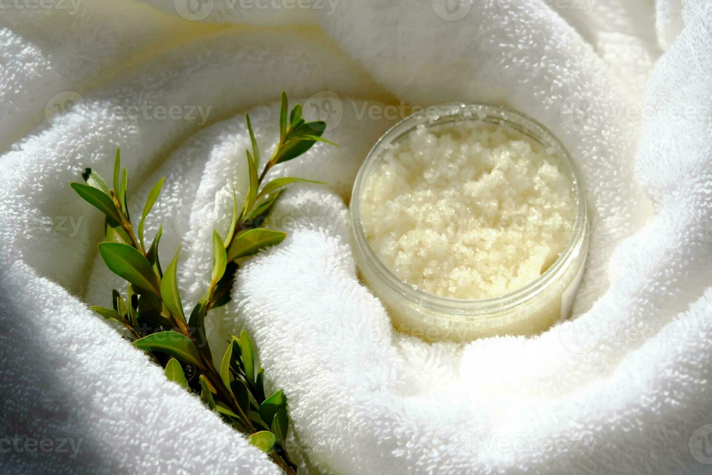 A jar of scrub wrapped in a terry bath towel with a green sprig. photo