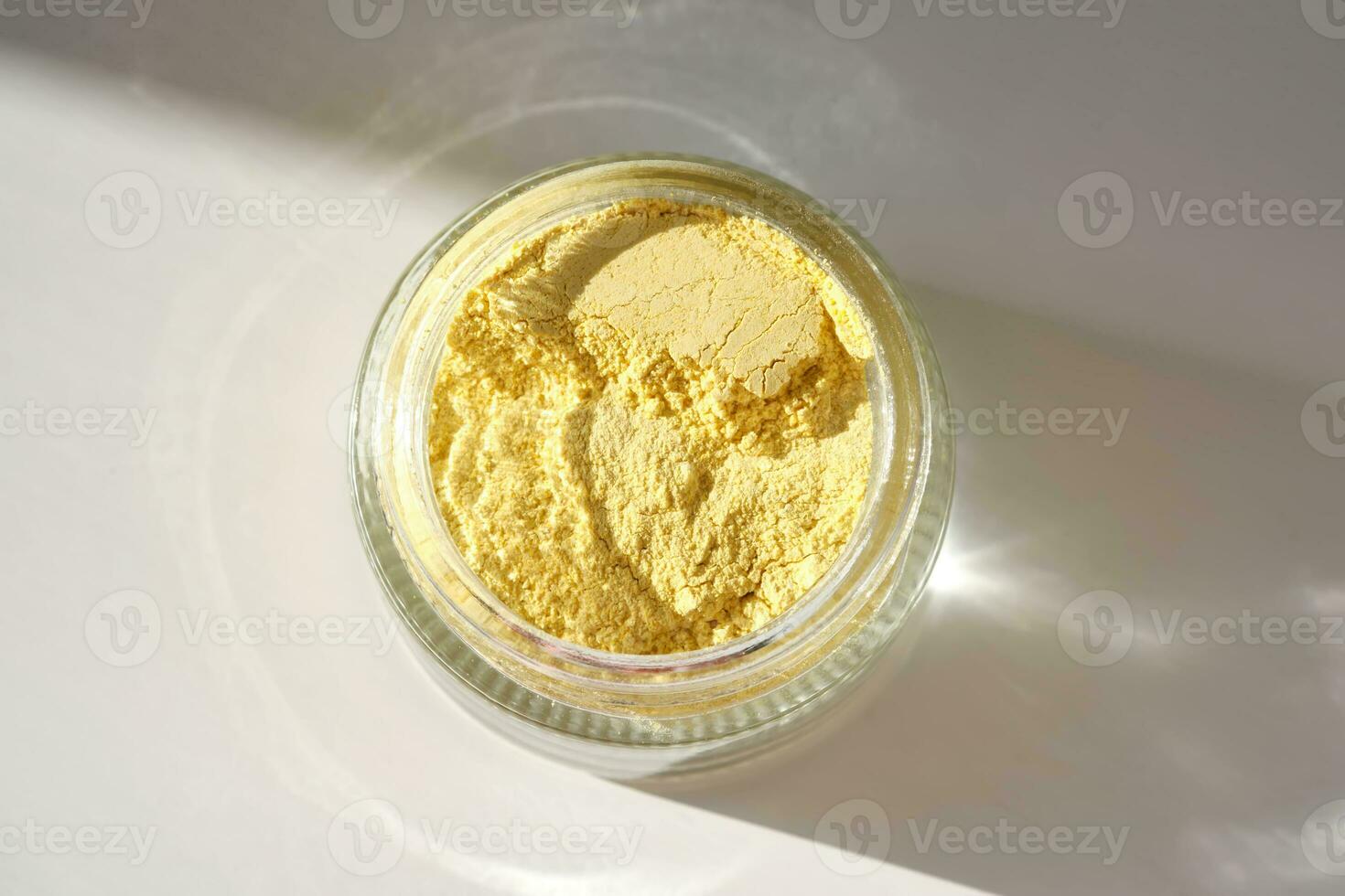 An open jar of a yellow turmeric facial scrub showing off its texture. photo
