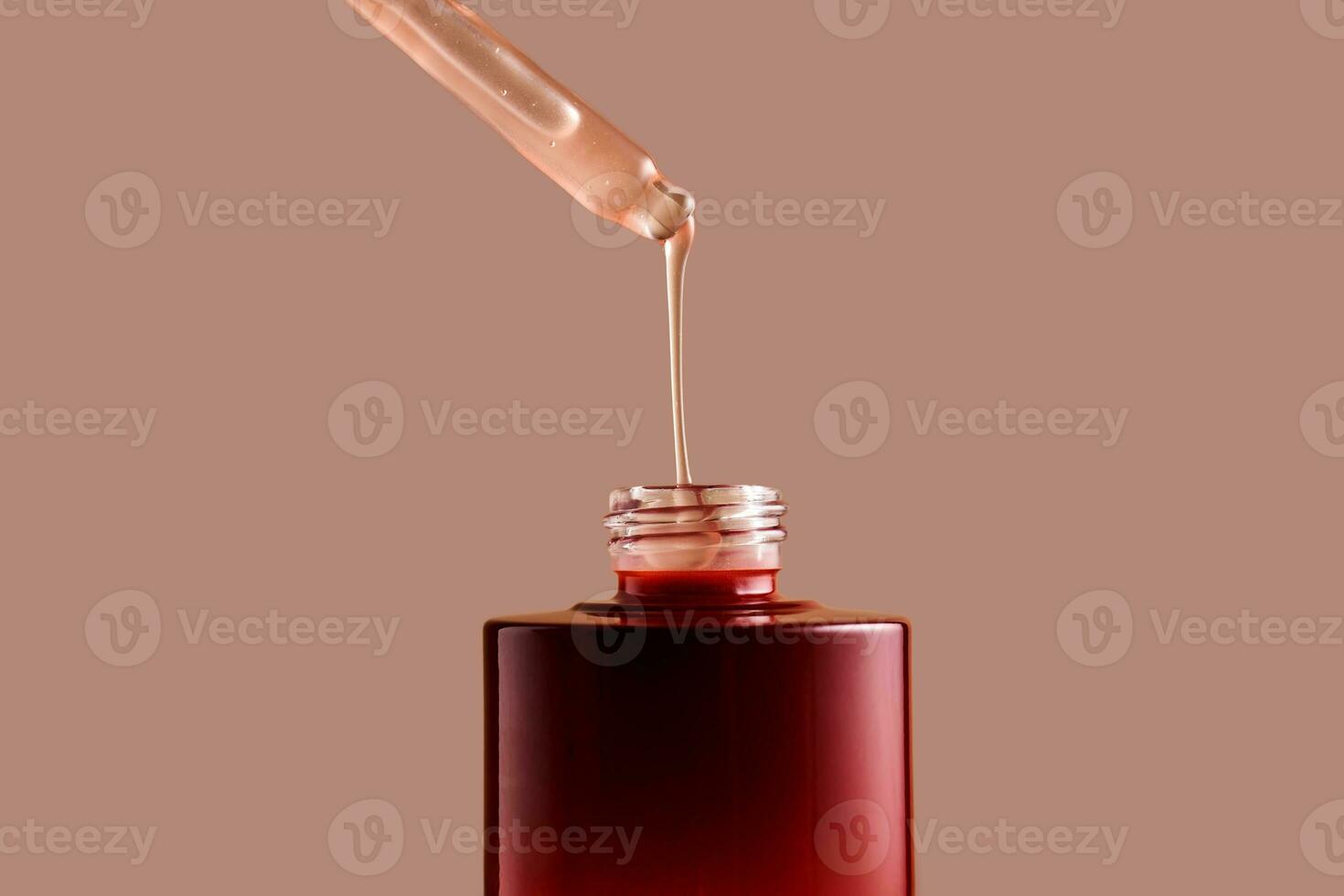 A drop of pink cosmetic drips from the dropper. photo