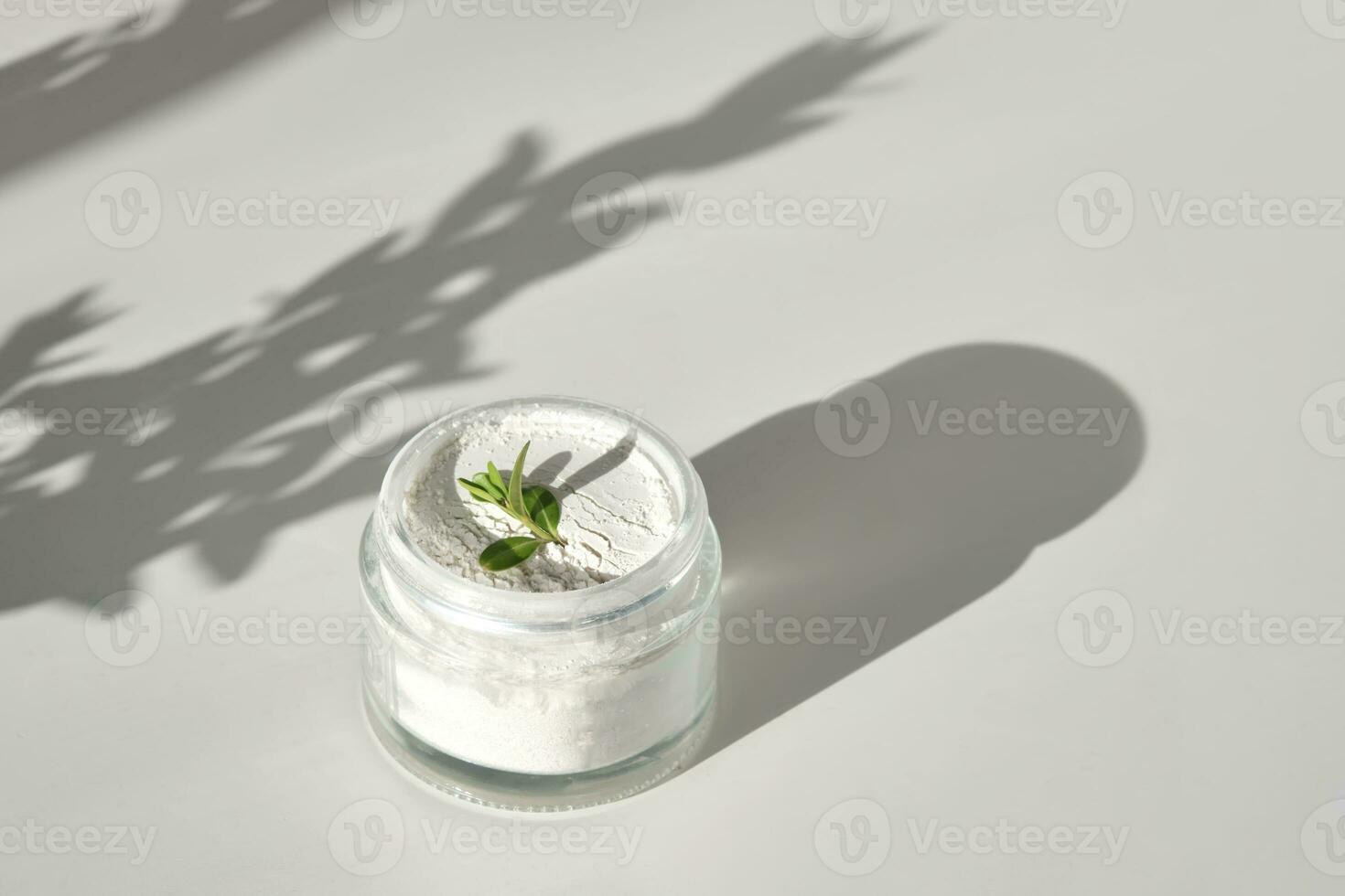 An open jar of facial scrub powder with a green sprig. photo
