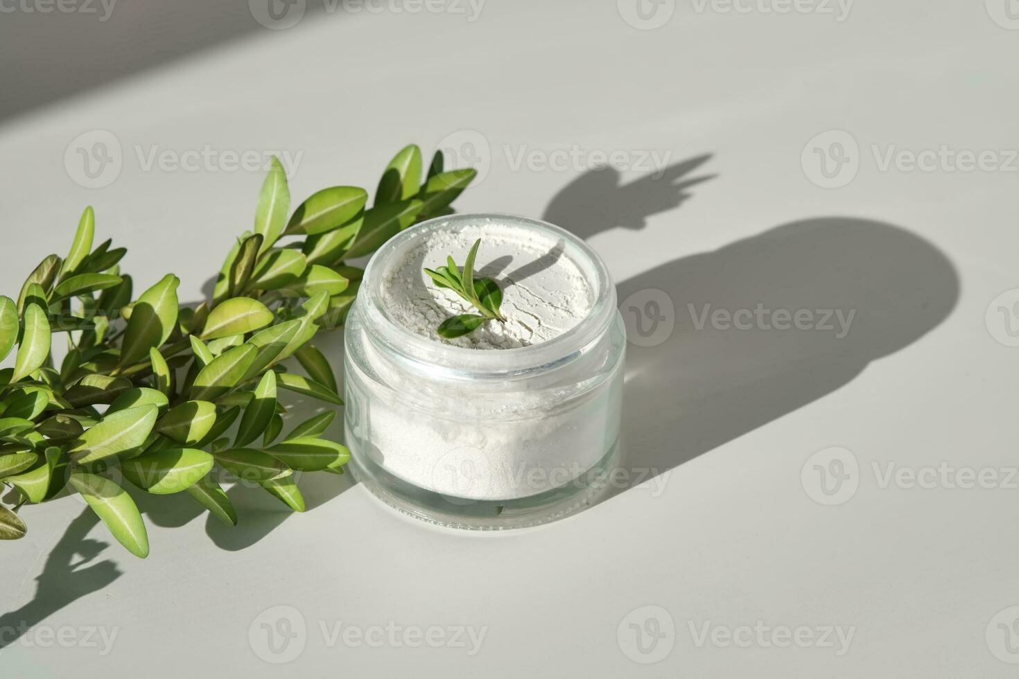 An open jar of facial scrub powder with a green sprig. photo