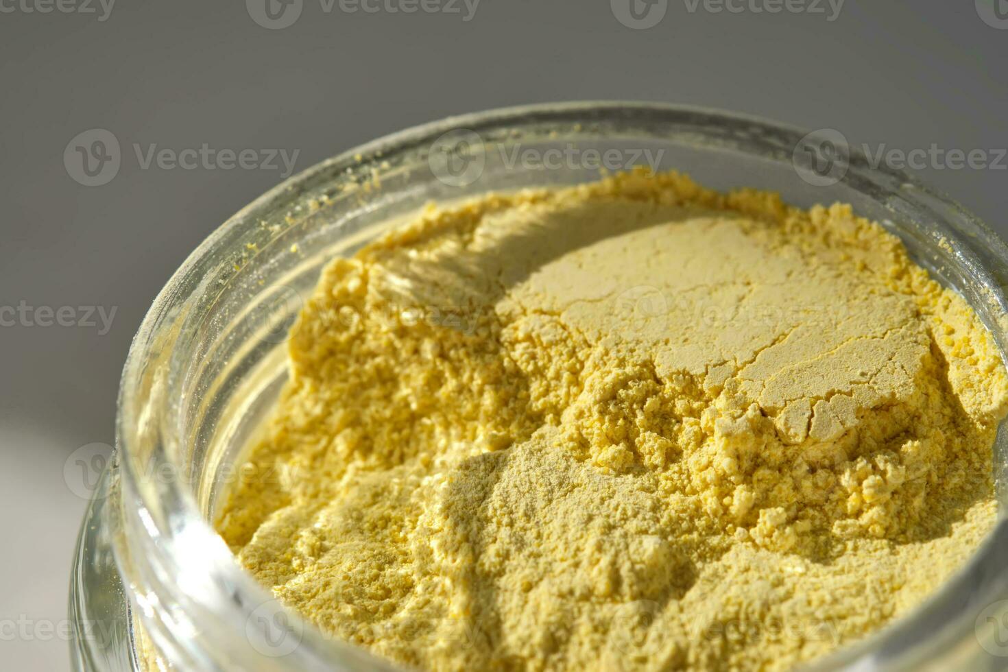 An open jar of a yellow turmeric facial scrub showing off its texture. photo