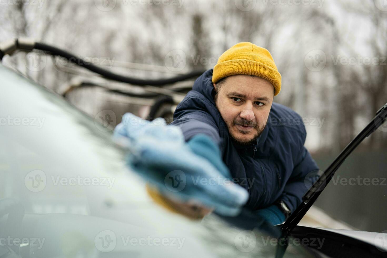 Man wipes american SUV car windshield with a microfiber cloth after washing in cold weather. photo