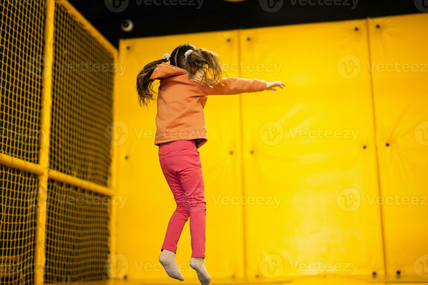 Little girl kid jumping on trampoline at yellow playground park. Child in motion during active entertaiments. photo