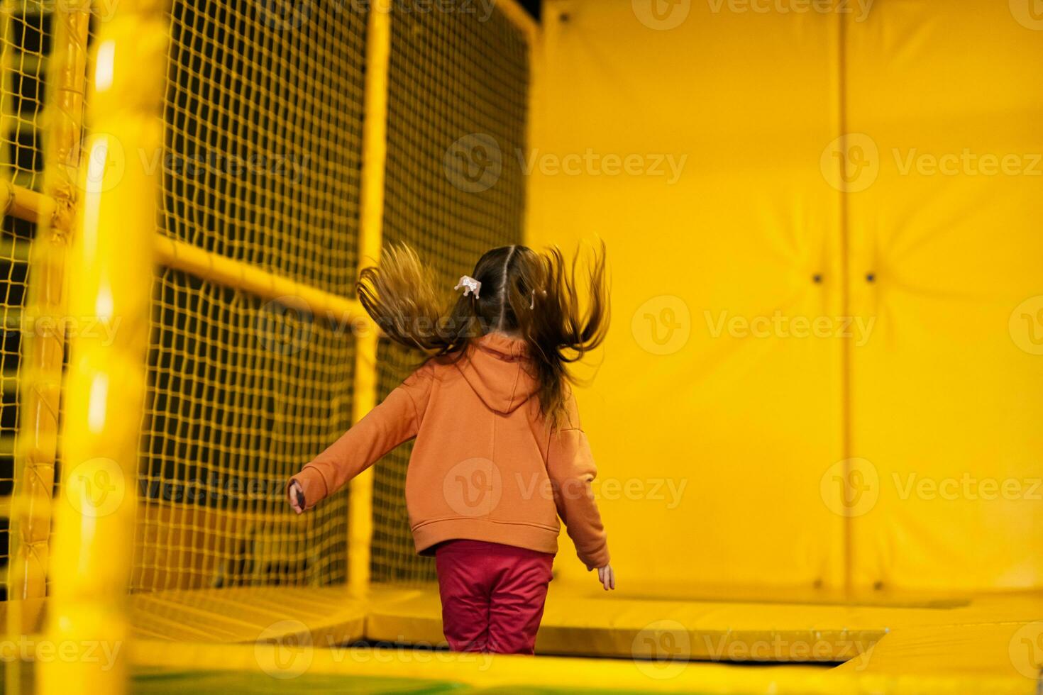 Little girl kid jumping on trampoline at yellow playground park. Child in motion during active entertaiments. photo