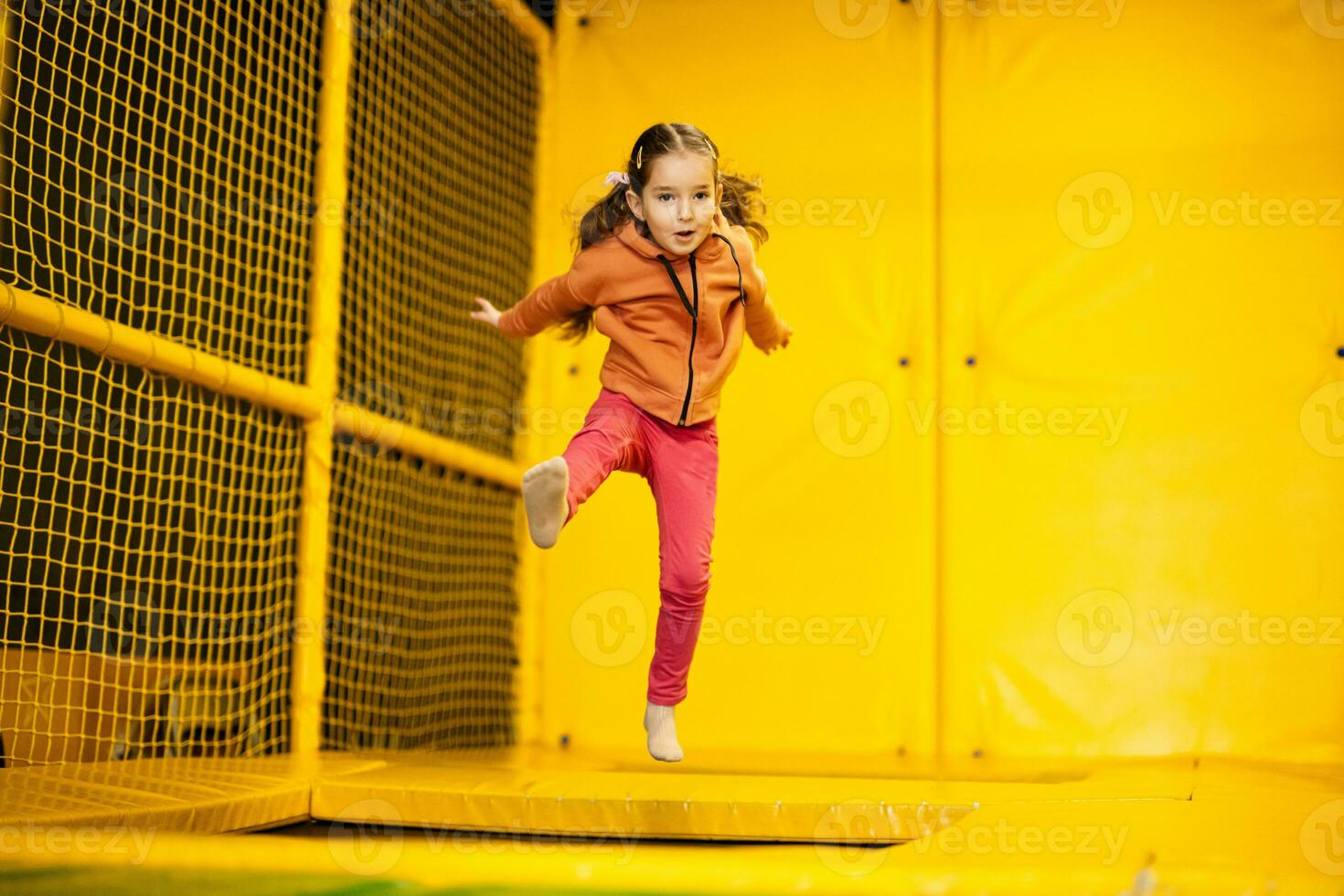 Little girl kid jumping on trampoline at yellow playground park. Child in motion during active entertaiments. photo