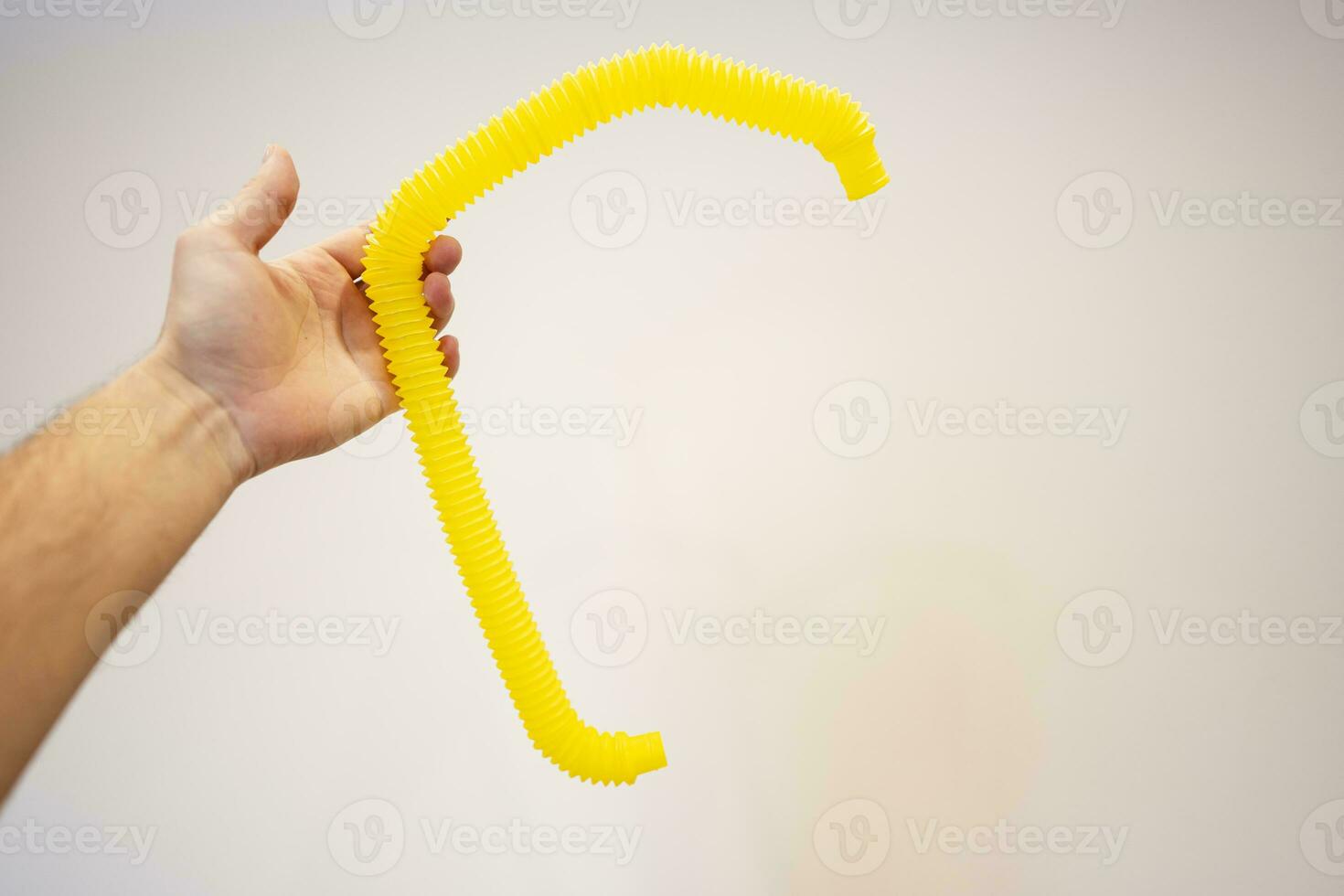 Male hand holding a yellow plastic tubule in front of a wall photo