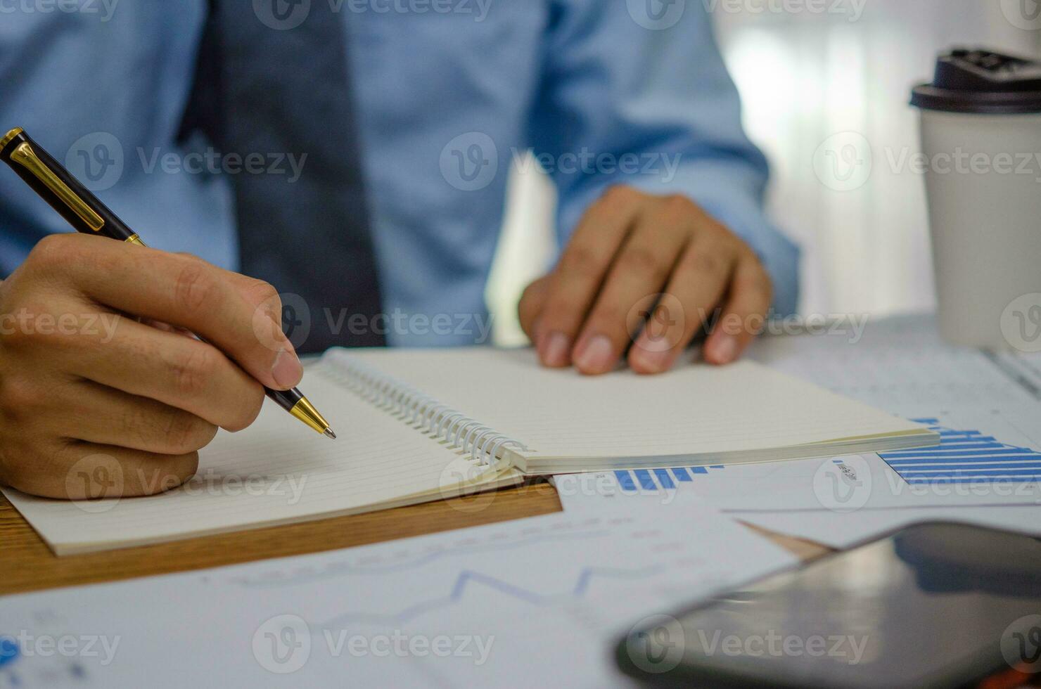 Businessman using pen writing note book planning journal and analysis information statistics document on desk. photo
