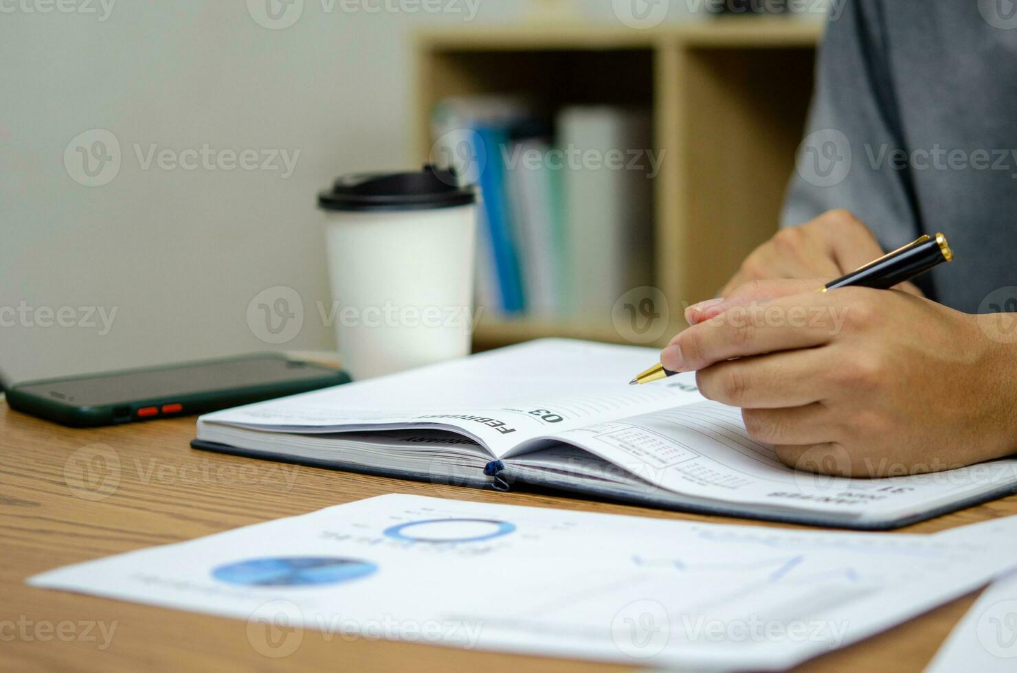 Businessman using pen writing note book planning journal and analysis information statistics document on desk. photo