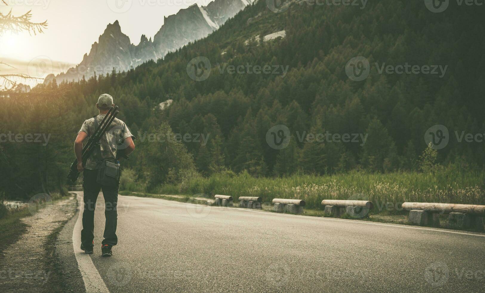 Photographer with Camera and Tripod Walking Along Mountain Road photo