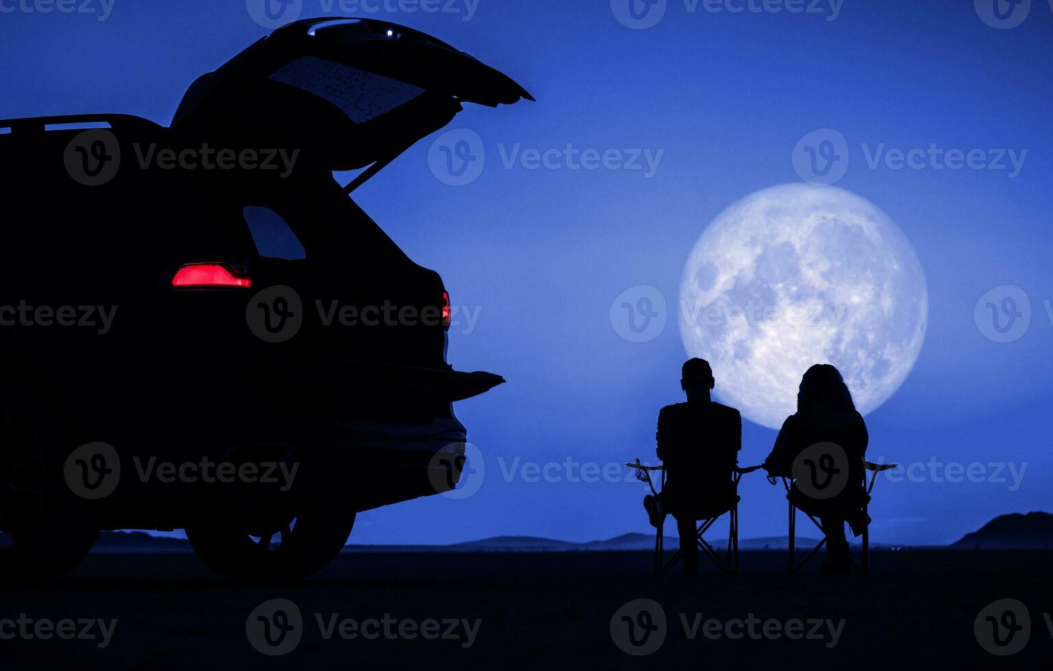 Couple Seating Next to Their Vehicle and Enjoying Full Moon Vista photo