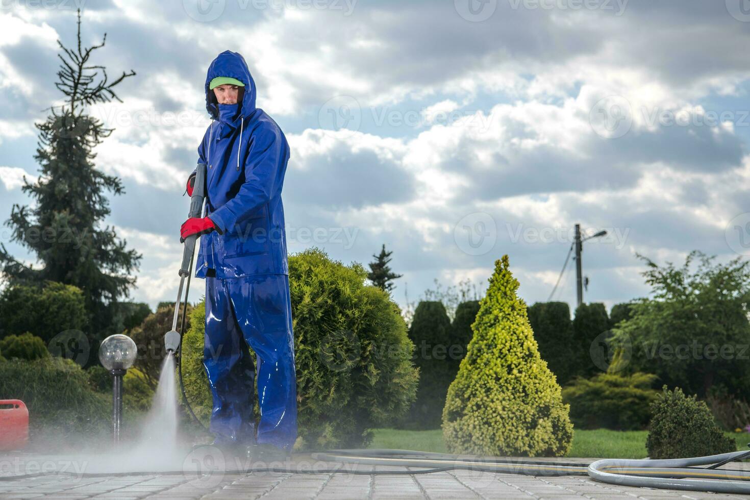 Male Groundkeeper Cleaning Sidewalk With High Pressure Equipment. photo