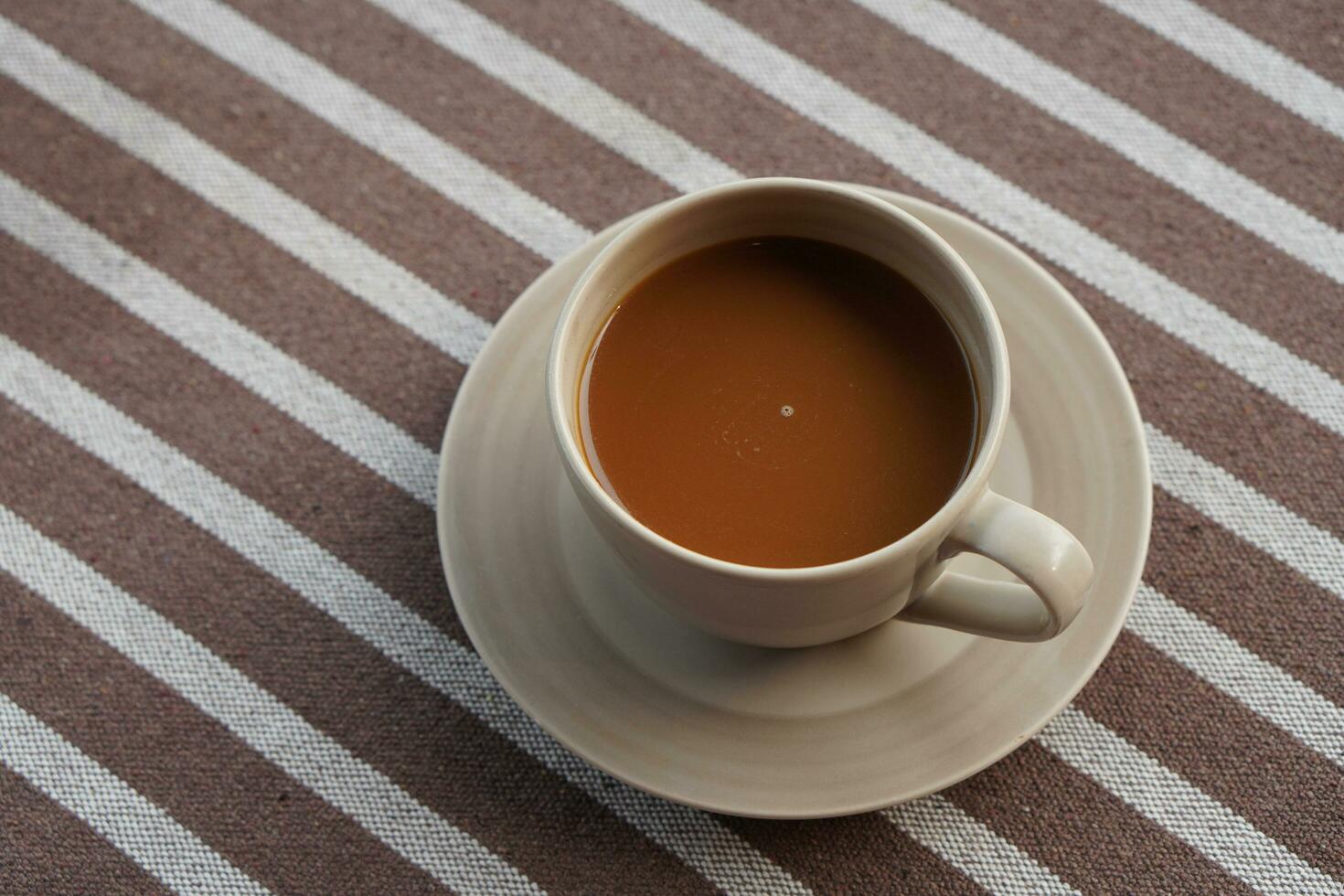 coffee in a pottery cup and silver spoon on a pottery coaster on brown and white fabric background, drink, food, health, copy space photo