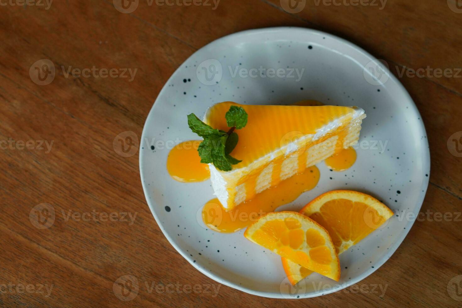 top view orange cake, with orange Jams decorated by a two piece of half cycle orange slides and green leaf put on a white ceramic plate on wooden floor background, fruit, food, ature, copy space photo