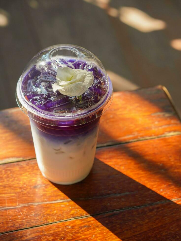 top view butterfly pea milk in a clear plastic glass, placed on a wooden table, on blur nature background photo