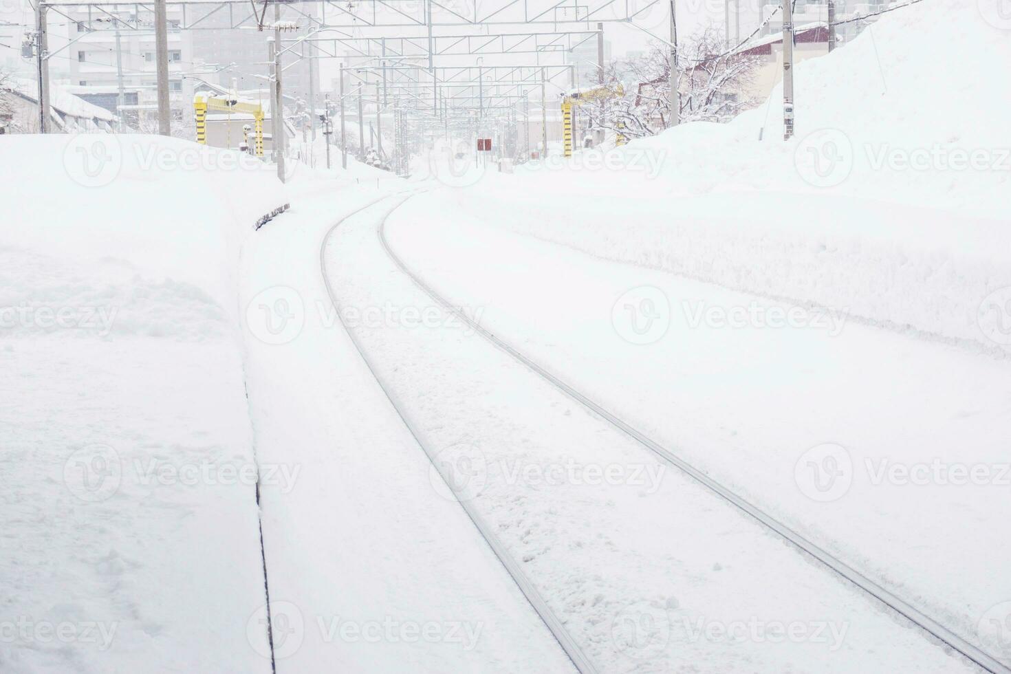 Cityscape view and closeup metal long railroad track in winter season and snow capped city with fully white foggy from snow storm background. photo