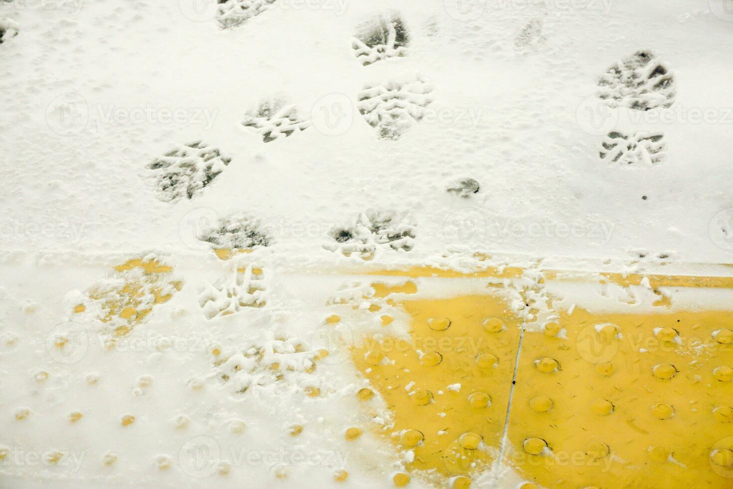 Image of snow and ices with texture of shoe and sneakers soles covered on floors and yellow braille code brick floors background. photo