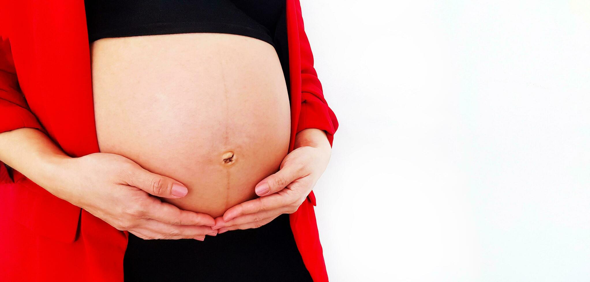 Close Up pregnant woman wearing  red suit holds hands on swollen belly isolated on white background and copy space with clipping path. Pregnancy 7-9 months, motherhood, love, expectation and car photo